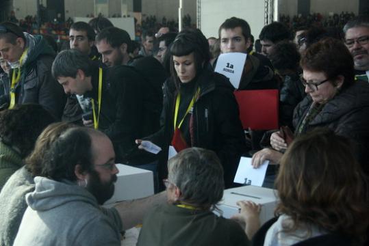 Dues inscrites a l'assemblea de la CUP es preparen per dipositar el seu vot a l'urna mentre un noi sosté amb la boca la papereta de la primera ronda. 