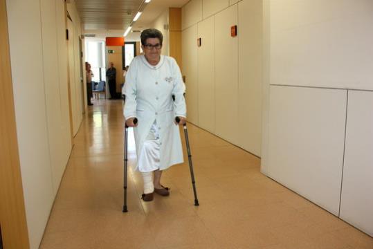 La pacient Carmen Moya operada, a l'Hospital Santa Maria de Lleida, camina amb crosses per un passadís. ACN